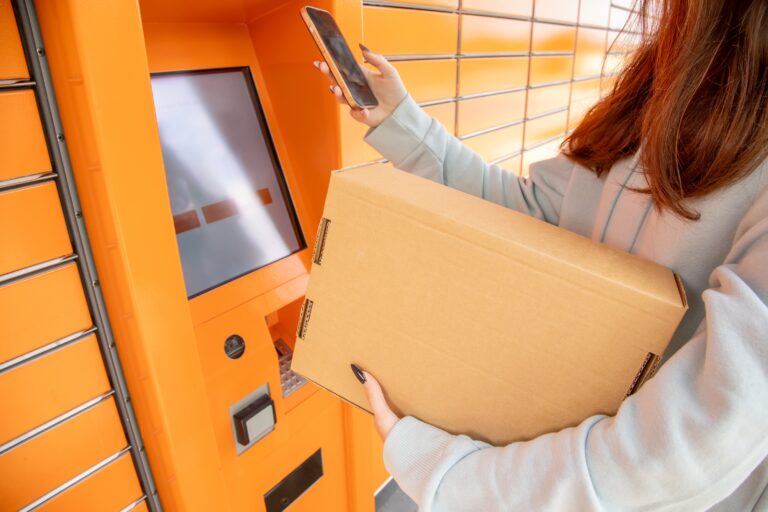 Woman holding a cardboard package while scanning a QR code on her phone at an orange automated parcel locker.