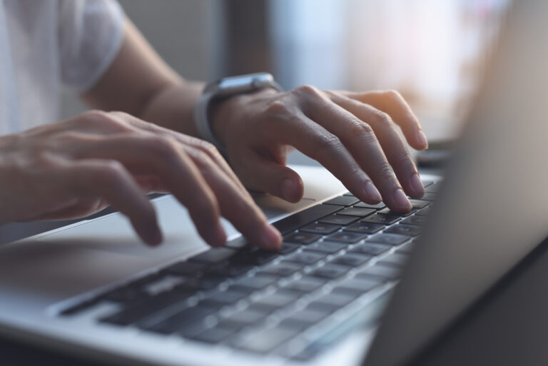 Close-up of hands typing on a laptop keyboard while writing an Amazon product title